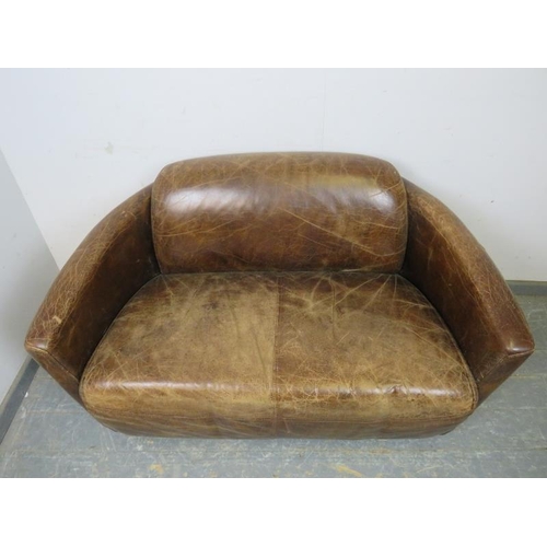 708 - A small two-seater sofa in the aviator style, upholstered in distressed brown leather, on block feet... 