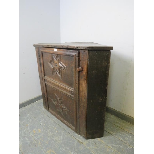 835 - A 17th century oak corner cupboard, the panelled door carved with star decoration in high relief, op... 