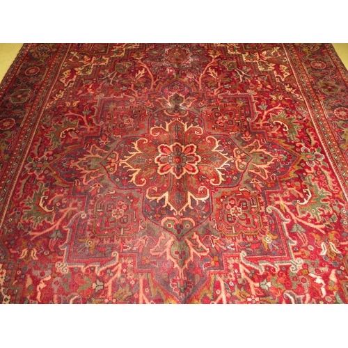 852 - A Northwest Persian Heriz carpet, central floral motif on deep red ground and wide borders.  290cm x... 