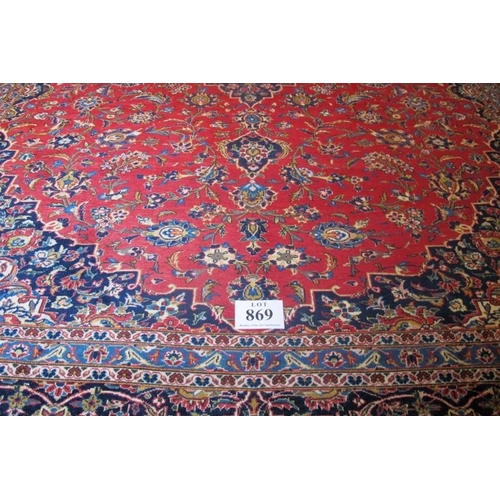 869 - A mid 20th Century Persian Kashan carpet.  Central motif, blue on red ground.  372cm x 283cm approx.... 