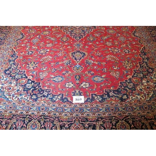 869 - A mid 20th Century Persian Kashan carpet.  Central motif, blue on red ground.  372cm x 283cm approx.... 