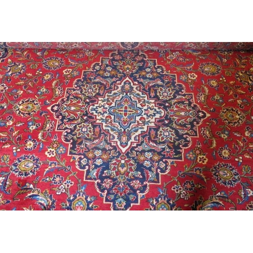 869 - A mid 20th Century Persian Kashan carpet.  Central motif, blue on red ground.  372cm x 283cm approx.... 