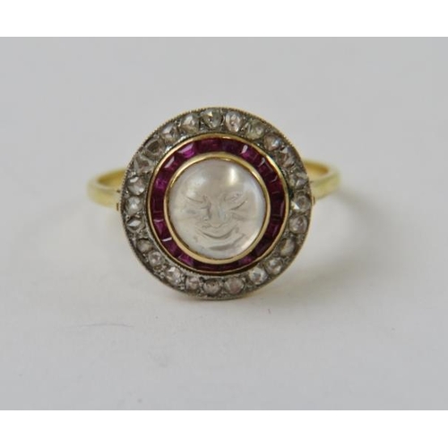 543 - A carved moonstone, ruby and diamond target dress ring, depicting a smiling face on the round moonst... 