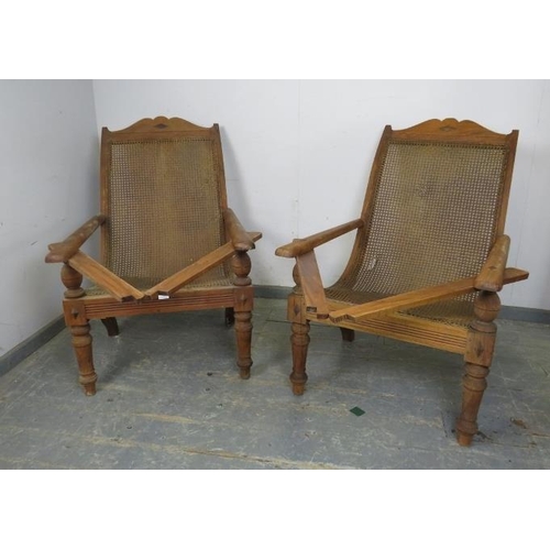 735 - A pair of early 20th century teak plantation chairs, having bergère seats and swing-out interlocking... 