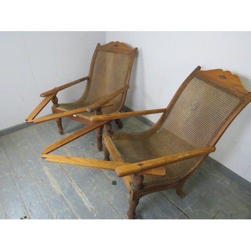 735 - A pair of early 20th century teak plantation chairs, having bergère seats and swing-out interlocking... 