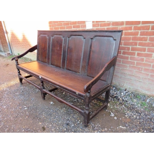 786 - An 18th century oak settle, the back with fielded panels joined with sloping arms to a bench seat, o... 