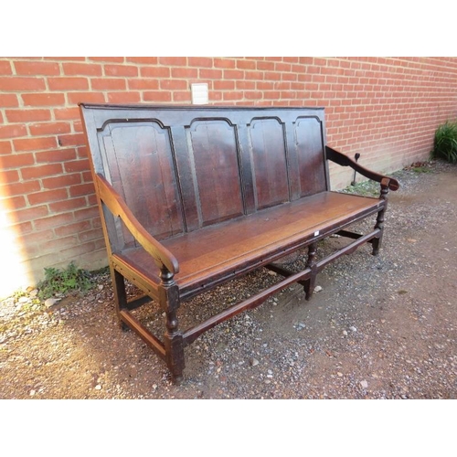 786 - An 18th century oak settle, the back with fielded panels joined with sloping arms to a bench seat, o... 