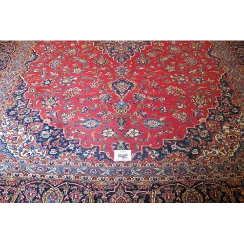 854 - A mid 20th Century Persian Kashan carpet.  Central motif, blue on red ground.  372cm x 283cm approx.... 