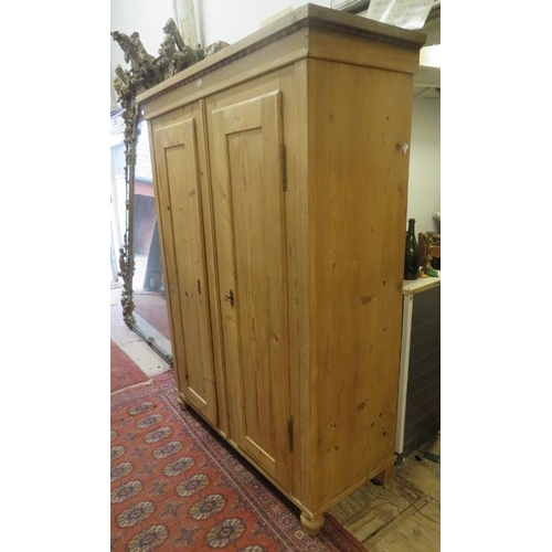 704 - A Continental stripped antique pine double wardrobe, the moulded cornice above two panelled doors op... 