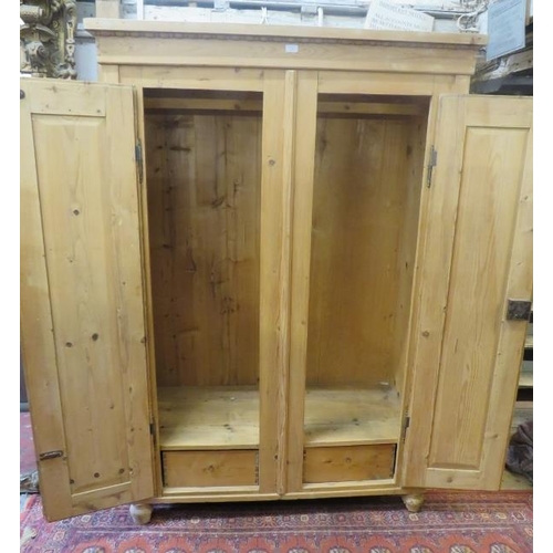 704 - A Continental stripped antique pine double wardrobe, the moulded cornice above two panelled doors op... 