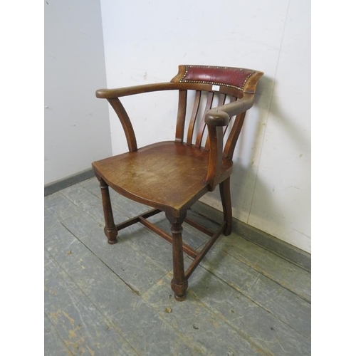 748 - A turn of the century oak captain’s chair, the backrest with antique claret leather with brass studs... 