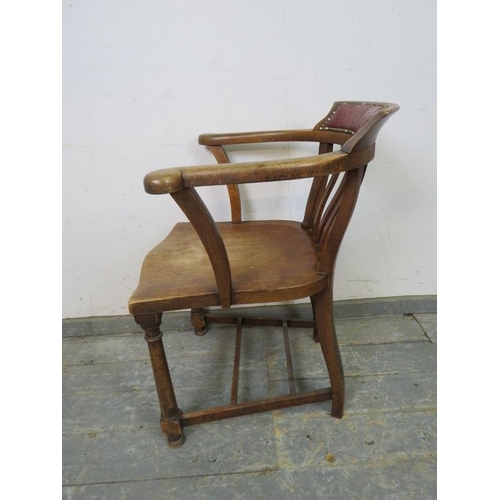 748 - A turn of the century oak captain’s chair, the backrest with antique claret leather with brass studs... 