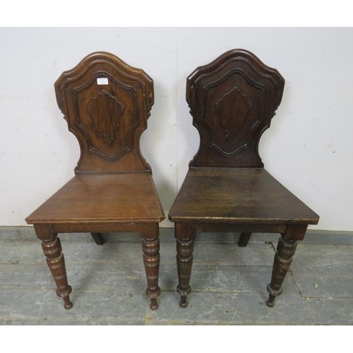 763 - A pair of Victorian oak hall chairs, the shaped backs with relief carved decoration, on tapered turn... 