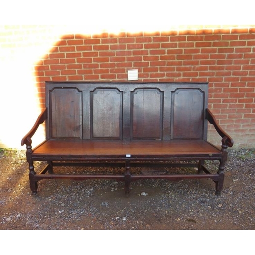 776 - An 18th century oak settle, the back with fielded panels joined with sloping arms to a bench seat, o... 