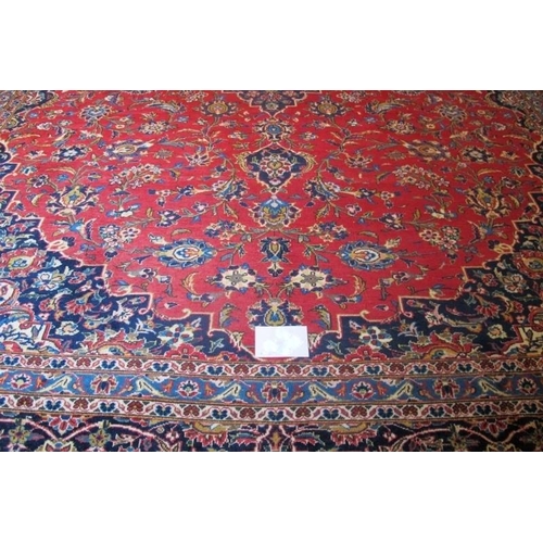 868 - A mid 20th Century Persian Kashan carpet.  Central motif, blue on red ground.  372cm x 283cm approx.... 