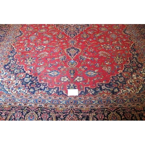 868 - A mid 20th Century Persian Kashan carpet.  Central motif, blue on red ground.  372cm x 283cm approx.... 