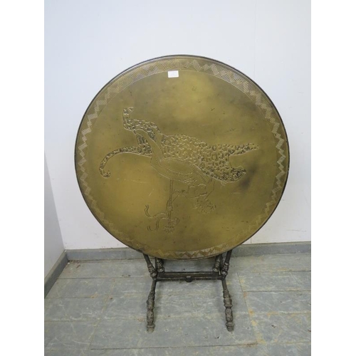 707 - An unusual brass topped folding table, the top with relief decoration depicting a man astride a leop... 