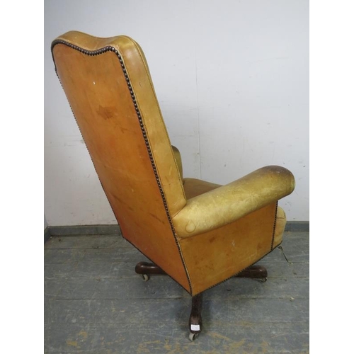 718 - A vintage high-backed revolving desk chair, upholstered in distressed tan leather with brass studs, ... 