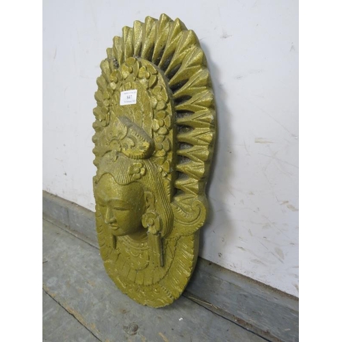 847 - A relief moulded concrete wall plaque painted gold, modelled as an Asian deity. 
H48cm W27cm D10cm a... 