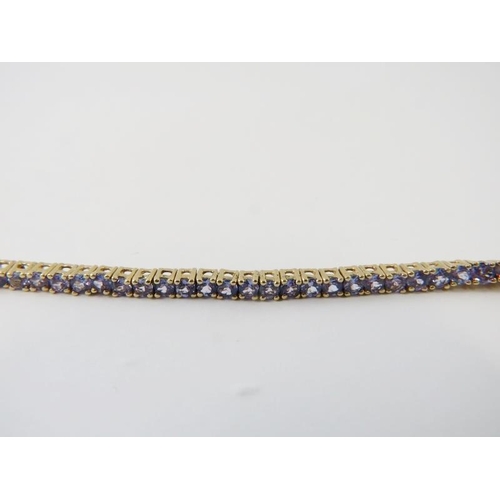 483 - A yellow metal and tanzanite line or tennis bracelet, the light purple round cut tanzanites measurin... 