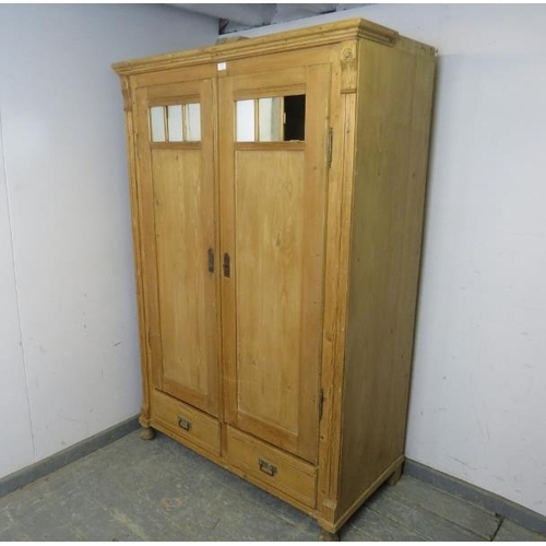 796 - An antique pine Continental double wardrobe, the twin doors with inset antiqued mirror panels, above... 