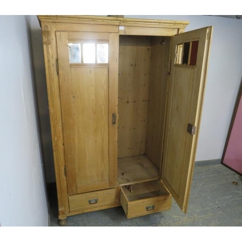 796 - An antique pine Continental double wardrobe, the twin doors with inset antiqued mirror panels, above... 