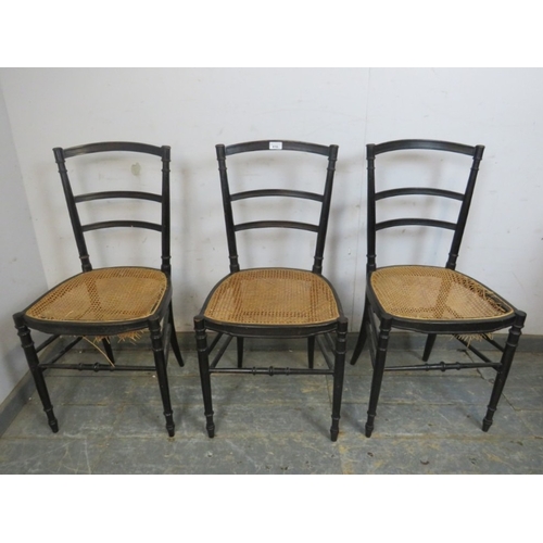 783 - A set of three 20th century ebonised ladderback dining chairs with rattan seats raised on turned and... 