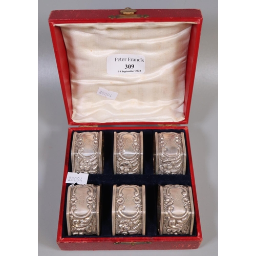 309 - Cased set of six silver repousse decorated octagonal napkin rings with 'C' scroll and flowerhead dec... 