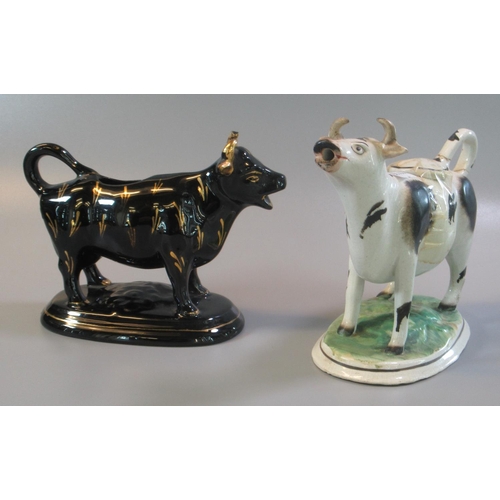 5 - Two 19th century pottery cow creamers, one black and white the other with black and gilt lustre deco... 