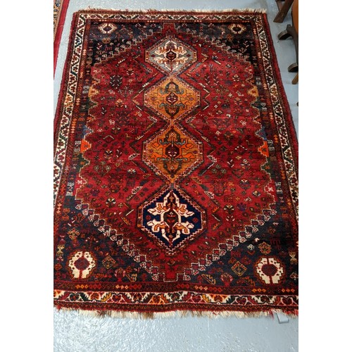 586 - Middle Eastern hand woven red ground carpet with four geometric and foliate medallions.  262x174cm a...