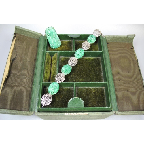 385 - A green leather cantilever jewellery box containing an Art Deco jade carved dress clip and a carved ... 