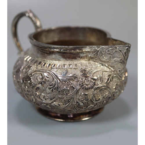 239 - White metal probably Indian baluster single handled cream jug with repoussé floral and foliate decor... 