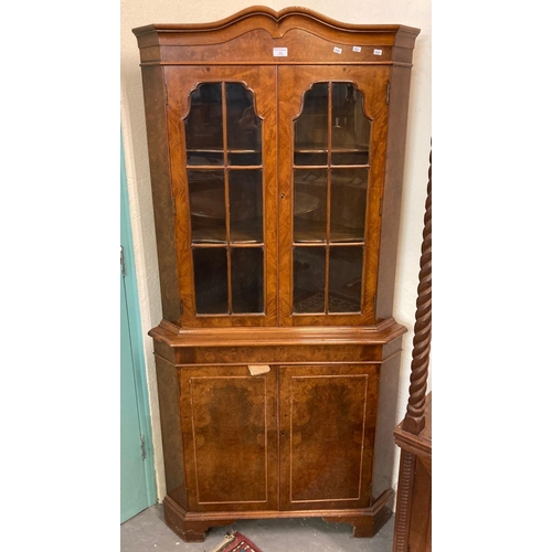 556 - Reproduction walnut two door glazed corner cabinet, the interior revealing shaped shelves.  (B.P. 21... 