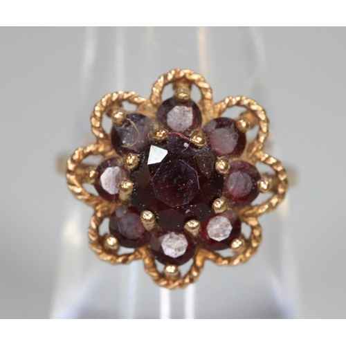 244 - Gold and garnet flowerhead dress ring.  Size L.  2.9g approx.  (B.P. 21% + VAT)