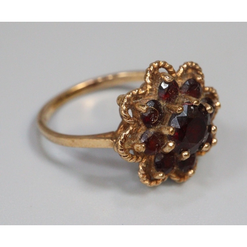 244 - Gold and garnet flowerhead dress ring.  Size L.  2.9g approx.  (B.P. 21% + VAT)