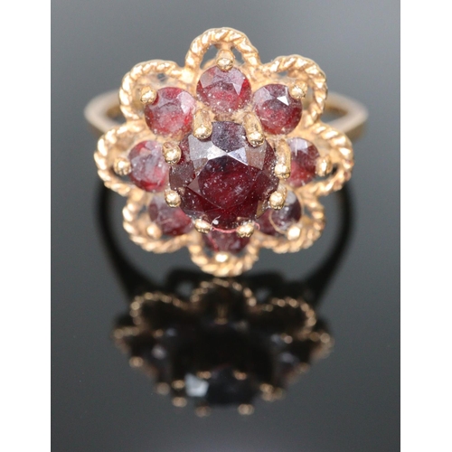 244 - Gold and garnet flowerhead dress ring.  Size L.  2.9g approx.  (B.P. 21% + VAT)