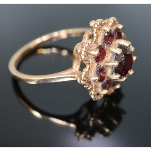 244 - Gold and garnet flowerhead dress ring.  Size L.  2.9g approx.  (B.P. 21% + VAT)