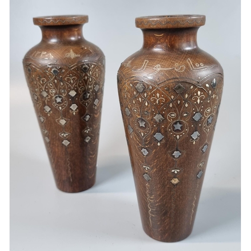 73 - A pair of unusual oak Islamic tapering vases inlaid with white metal stars, foliage and other decora... 