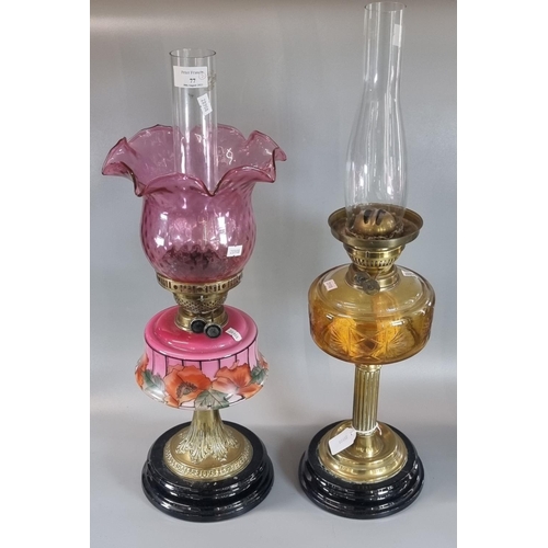 77 - Two early 20th century double burner oil lamps, one with cranberry coloured shade, clear chimney and... 