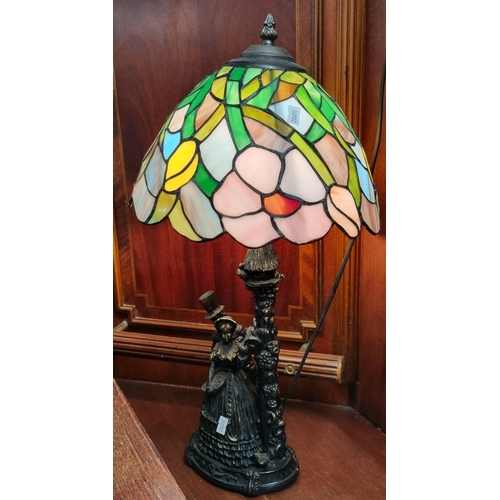 119 - Modern Tiffany style table lamp, the base with bronzed decoration of Victorian gent and lady with bi... 