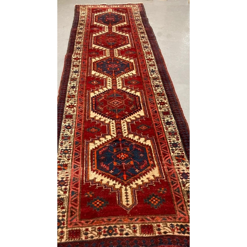 473 - Red ground Persian Heriz runner originating from Northern Iran with repeating central medallions, fl... 