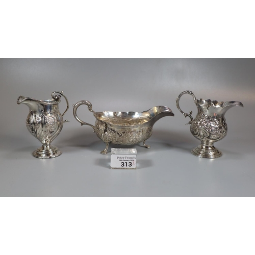 313 - Two similar silver repoussé helmet shaped cream jugs together with a similar silver sauce boat.  12.... 