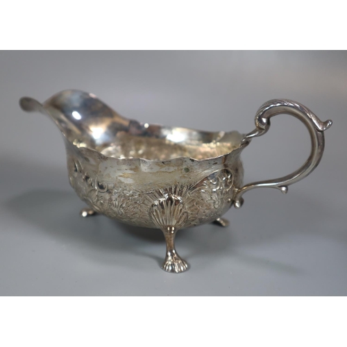 313 - Two similar silver repoussé helmet shaped cream jugs together with a similar silver sauce boat.  12.... 