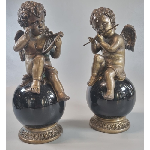 16 - Pair of bronze seated musical cherubs playing the flute and harp, on glass globular and gilded bases... 