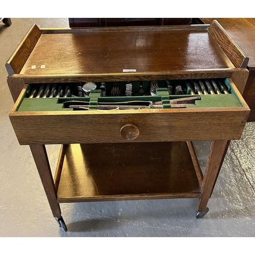 421 - Early 20th century oak two tier trolley on wheels, the pull out drawer with a collection of silver p... 