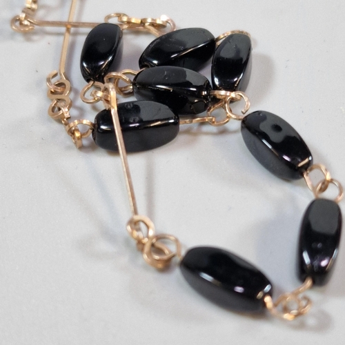 291 - Yellow metal and black polished stone necklace. 8.8g approx. (B.P. 21% + VAT)