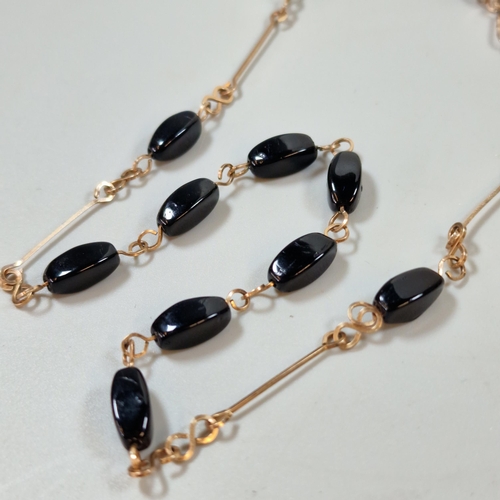 300 - Yellow metal and black polished stone necklace. 8.8g approx. (B.P. 21% + VAT)