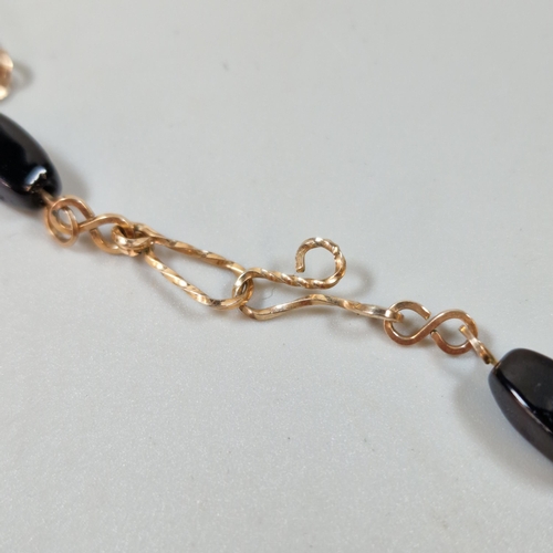 300 - Yellow metal and black polished stone necklace. 8.8g approx. (B.P. 21% + VAT)