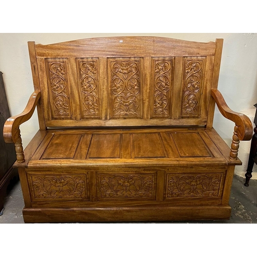 528 - Modern hardwood settle, the high back with four carved foliate panels, shaped open arms with hinged ... 