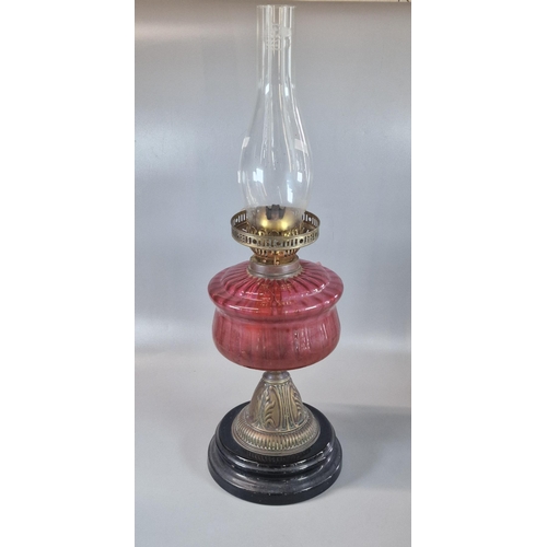 91 - Early 20th century double oil burner lamp having cranberry glass reservoir above a brass and ebonise... 